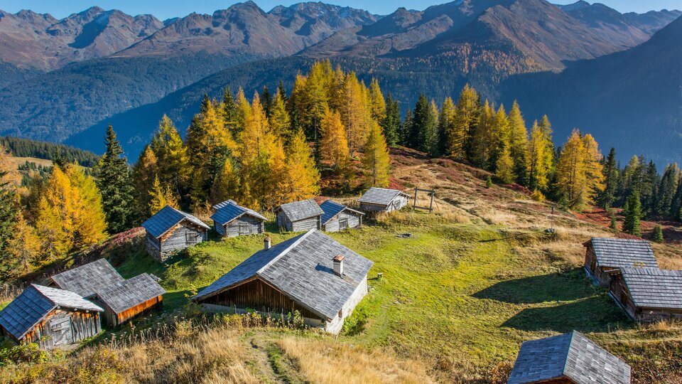 A picturesque mountain landscape with several huts and colorful autumn forest. Majestic mountains rise in the background.