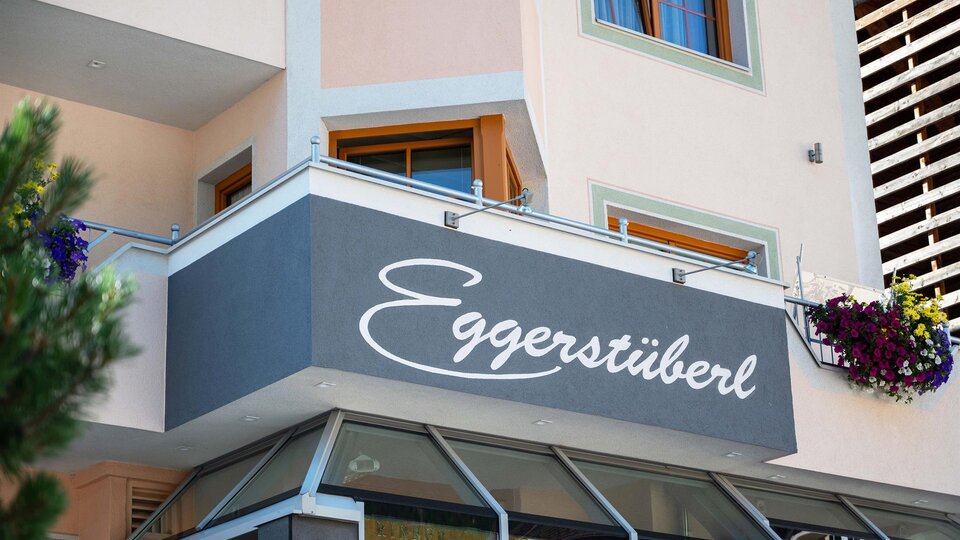 A modern building with a knit front and a large sign reading "Eggerstüberl". Flowers adorn the windows, giving the place an inviting atmosphere.