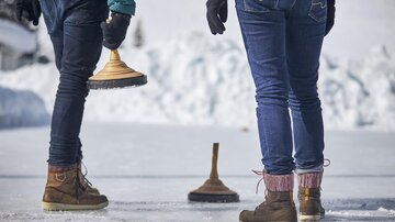 Two people are standing on a frozen surface holding curling stones. There is snow in the surroundings and the atmosphere is wintry. | © TVB Paznaun -  Ischgl