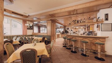 A cozy restaurant with wooden elements and a friendly atmosphere. The decor is elegant and inviting, with tables and bar stools.