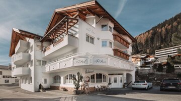 A modern hotel building with a distinctive roof and an inviting facade. It is located in a picturesque mountain landscape.