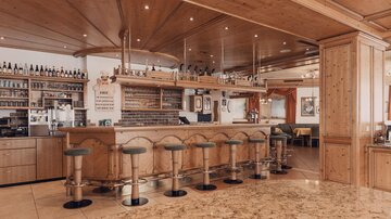 A cozy bar with wooden design and stools. In the background, shelves with drinks can be seen.