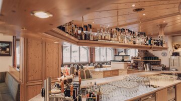 An elegant bar with wooden elements and an extensive selection of spirits. Glasses are neatly arranged on the counter area.