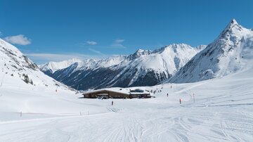 A picturesque winter landscape with snow-covered mountains. In the foreground, there are ski slopes and a cozy mountain cabin.