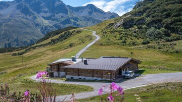 A modern wooden house in a picturesque mountain landscape. Surrounded by green meadows and tall mountains, the environment offers a calm and relaxing atmosphere.
