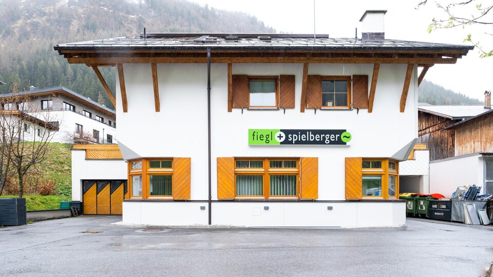 A modern building with a white exterior paint and wood cladding. The logo of "fiegL spielberger" is prominently displayed above the entrance.