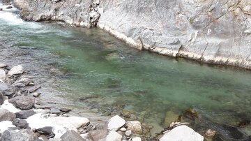 A clear river flows between rocky shores. The water is greenish and the surroundings are shaped by rocks.
