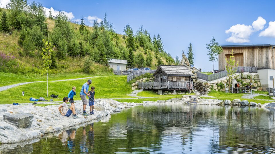 A tranquil lake surrounded by green meadows and trees. Children and adults enjoy nature and spend time by the shore.