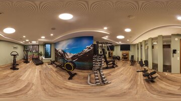 A modern gym with various workout machines and an inspiring mountain landscape on the wall. The room is bright and inviting, perfect for a workout.