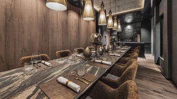 An elegant dining room with a long table and comfortable chairs. The atmospheric lighting and the wood-paneled walls create a cozy atmosphere.
