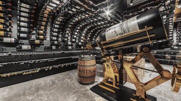An elegant wine cellar with many wine bottles on the walls. In the center stands a large wine pillar together with a wooden barrel.