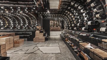 An elegant wine cellar with wall-filling wine bottles. The floor is made of stone and there are wooden boxes for storage.