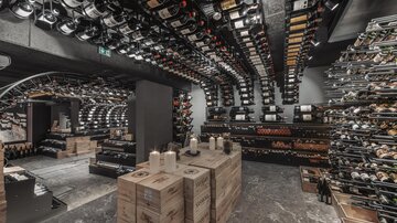 A tastefully furnished wine cellar with shelves full of wine bottles. In the center, there are wooden crates and candles create a cozy atmosphere.
