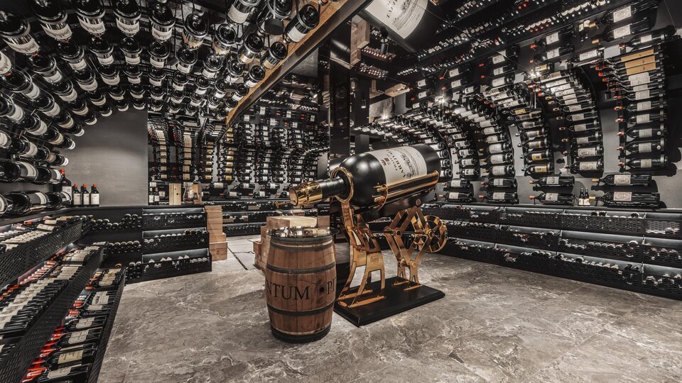 A stylish wine cellar with shelves full of wine bottles. In the center stands a wine barrel and an elegant wine press.