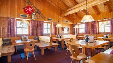 A cozy restaurant with wooden furniture and a warm atmosphere. Large windows provide plenty of daylight.