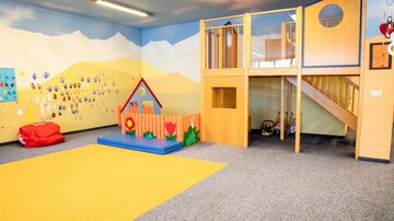 A bright and cheerful playroom with colorful walls. There is a play area with a small slide and a cozy seating area.