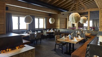A modern restaurant with wooden decor and a cozy atmosphere. The tables are elegantly set and large windows provide a view outside.