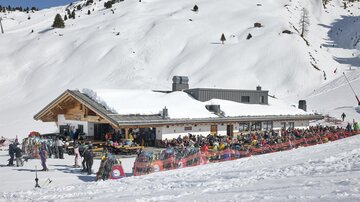 A ski resort with a large, snow-covered building. Many people are gathered outside and enjoying the winter day.