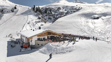 A ski chalet surrounded by snow-capped mountains. Many people are enjoying the sun and the winter atmosphere.
