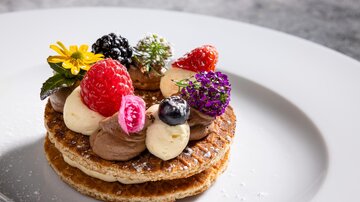 An artistic dessert with crispy waffles, chocolate cream, and colorful berries. Fresh edible flowers add a special touch to the dish.