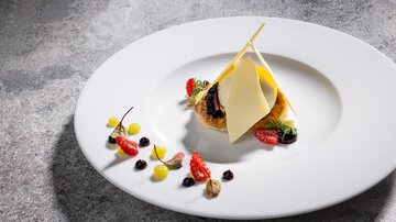 An artfully arranged plate with a delicious dish that includes fresh berries and a layer of cheese. The decoration features colorful fruit purees that make the plate visually appealing.
