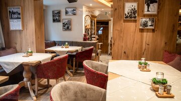 A cozy restaurant with wooden walls and red chairs. There are small plants and candles on the tables.