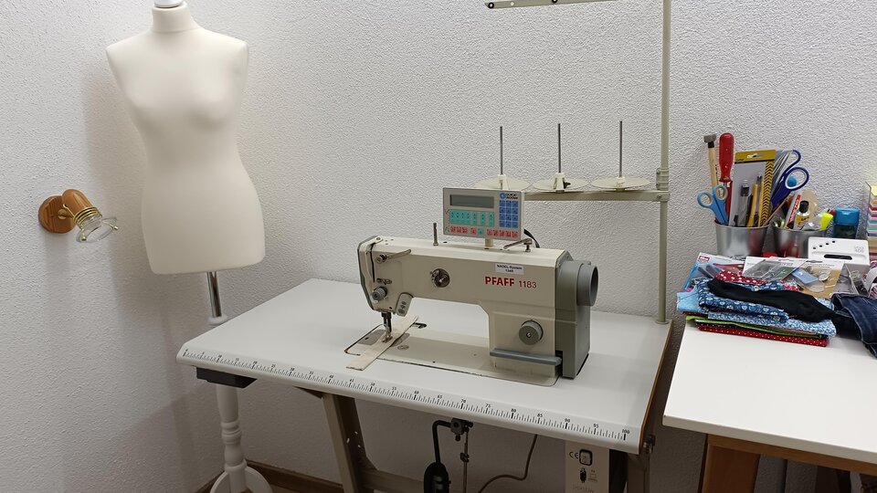 A bright sewing room with a sewing machine and a dress form. Various sewing tools and fabrics are visible on the table.