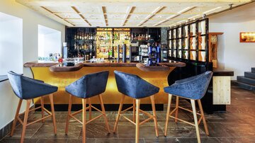 An elegant bar with modern bar stools and a well-stocked drink selection. The lighting creates an inviting atmosphere.