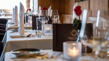 An elegantly set table in a restaurant. The table decoration includes white napkins, glasses, and red roses.