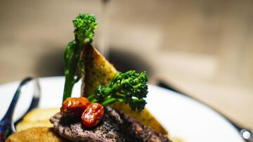A delicious plate with grilled steak, a schnitzel, and colorful vegetables. In the background, there is a glass of red wine.