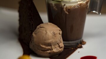 An elegant dessert with a chocolate cup, whipped cream, and fresh mint. Next to it lies a chocolate ice cream and a piece of cake on an artistically decorated plate.