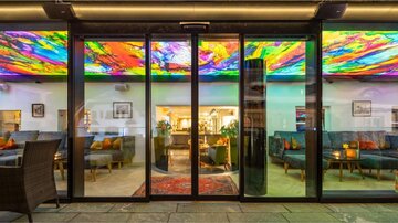 A modern café with stylish seating and a colorful, vibrant ceiling mural. The atmosphere is inviting and cozy.