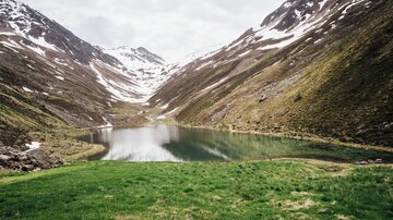 A tranquil mountain lake surrounded by snow-capped mountains and lush greenery. The clouds reflect the peaceful atmosphere of the landscape.