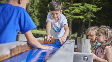 Children are playing at a water playground outdoors. They are having fun while experimenting with water and sand.