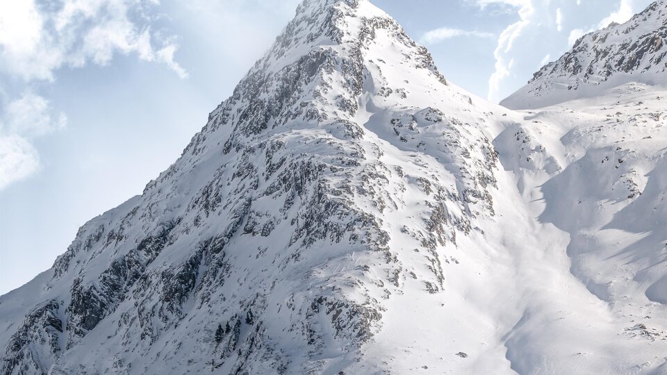 A majestic mountain with snow-covered slopes under a cloudy sky. The peaks are bathed in radiant sunlight.