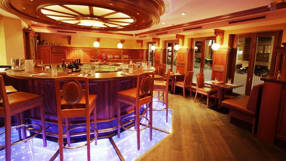 A stylish bar with wooden paneling and a illuminated counter. Cozy seating completes the inviting atmosphere.