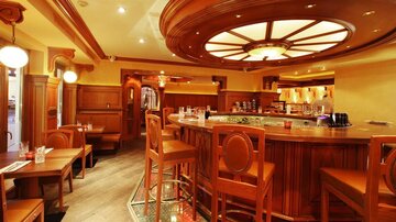 A stylish bar interior design made of wood with elegant lighting. The bar is well-equipped and inviting, with cozy seating options.