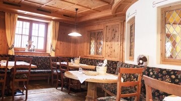 A cozy restaurant with wooden paneling and traditional tables. The decor is rustic with comfortable benches and windows with stained glass.
