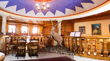 A cozy restaurant with rustic decor and a colorful ceiling pattern. A statue of a mountain animal stands prominently in the room.