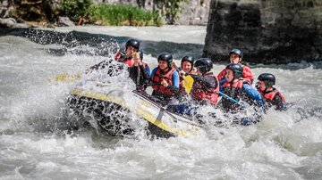 An exciting rafting tour on wild waters with multiple people in the boat. Everyone is wearing helmets and life jackets.