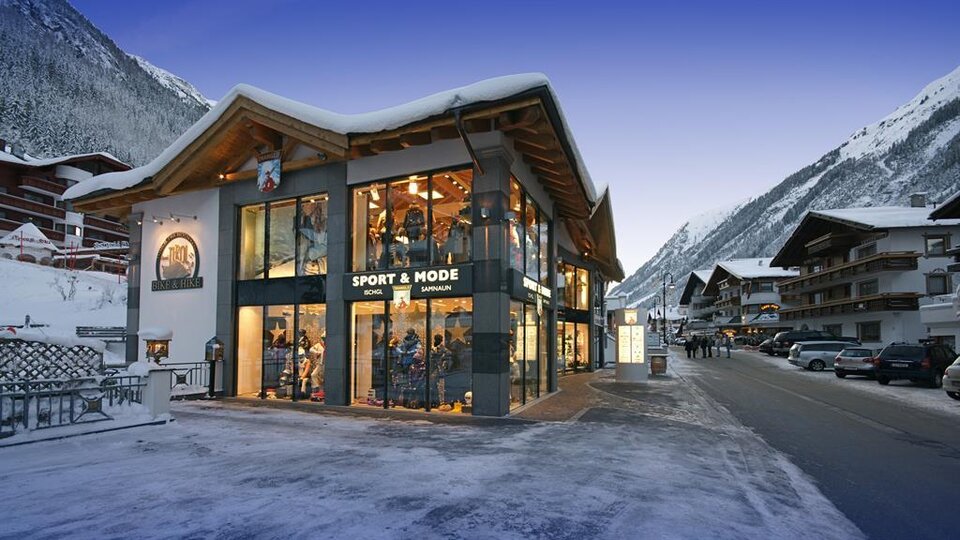Ein modernes Geschäft in den Alpen, umgeben von schneebedeckten Bergen. Die Fassade ist großflächig verglast und einladend.