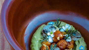 Eine kunstvoll angerichtete Speise in einer braunen Schüssel. Die Zutaten sind mit frischen Kräutern und essbaren Blumen garniert.