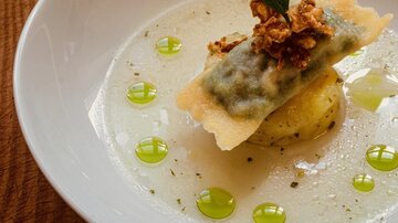 Ein elegantes Gericht serviert in einer weißen Schüssel. Es besteht aus Ravioli mit einer Füllung, garniert mit knusprigen Zwiebeln und grünen Tropfen.