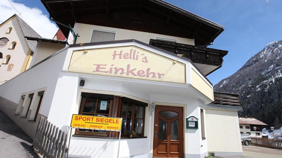 A cozy inn called "Hell's Einkehr" in the mountains. The facade is designed in a friendly manner and there is a view of the surrounding mountains.