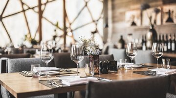 An elegant restaurant with stylish table arrangements. Glasses and cutlery are set, and a floral decoration gives the ambience an inviting touch.