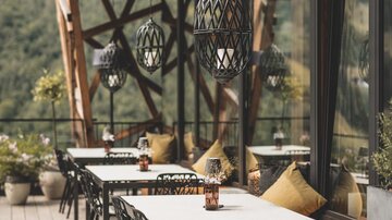 A cozy outdoor area of a restaurant with wooden decks and modern furniture. The tables are set for guests, and there are decorative plants.