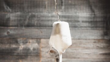 A hand pours champagne into a glass while the liquid overflows. The scene has a rustic wooden surface in the background.
