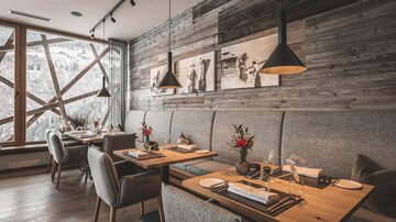 An elegant restaurant with wooden walls and cozy tables. Large windows offer views of the snowy landscape.