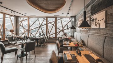 A modern restaurant with wooden decor and large windows. The space is stylishly decorated and offers a view of the snowy landscape.