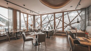 A modern restaurant with large windows and a view of the mountains. The decor is stylish and cozy, with wood and fabric elements.